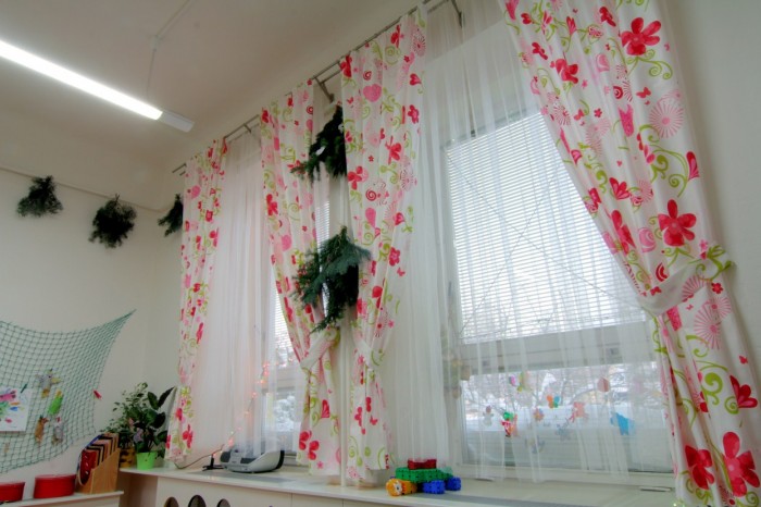 TYTO ZÁVĚSY se stylizovanými růžovými kytičkami a motýlky okno doslova rozzáří. Za oknem je sníh, v pokojíku této mateřské školy se ale děti dívají na rozkvetlou louku.